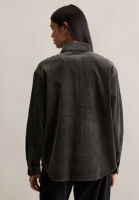 Szara koszula ze sztruksu z kołnierzykiem, długimi rękawami i luźnym krojem. Widoczna prążkowana faktura z lekko zaokrąglonym dołem.