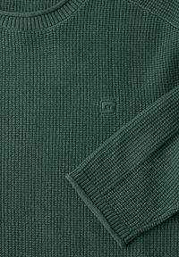 Tmavě zelený žebrovaný svetr s pletenou texturou, kulatým výstřihem a malou nášivkou s logem. Manžety a lem mají odpovídající žebrovaný vzhled.