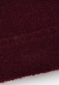 Tecido de malha bordeaux com uma textura suave e peluda. Apresenta um logótipo bordado "Levi's" sutilmente integrado no design.