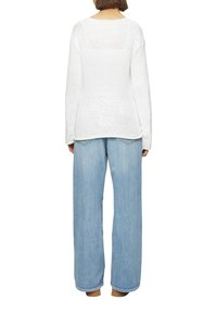 Witte gebreide trui met een losse pasvorm, voorzien van een textuurpatroon. Gepaard met lichtblauwe wijde jeans, beide casual in ontwerp en kleur.