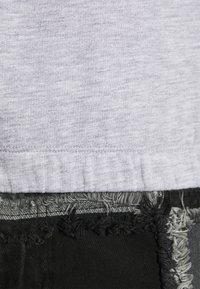 Gros plan sur un tissu gris clair superposé à un tissu noir avec des bords effilochés et des coutures visibles entre les deux textiles.