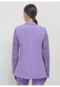 Fioletowa marynarka z koronkowymi rękawami, dopasowanym krojem i wyciętym kołnierzem. Gładka tkanina z fakturowanym wzorem koronki na rękawach.