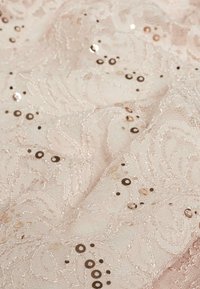 Spitzenstoff in sanftem Rosa mit floralem Muster, verziert mit bronzefarbenen und goldenen Pailletten, die eine strukturierte, dekorative Oberfläche schaffen.