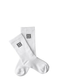 Białe bawełniane skarpetki o żebrowanej fakturze z czarnym logo na kostce. Zaokrąglony nosek z miękkim, elastycznym ściągaczem u góry.