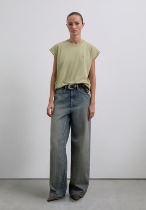 T-shirt vert clair à manches courtes, coupe ample. Jean bleu à jambes larges avec décoloration, taille haute. Ceinture noire avec un accent à motifs. Chaussures brunes à bout pointu.