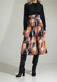 Černý dlouhý rukáv top s skládáním, geometricky vzorovaná sukně v oranžové, černé a šedé barvě, doplněná černými vysokými botami až po kolena.