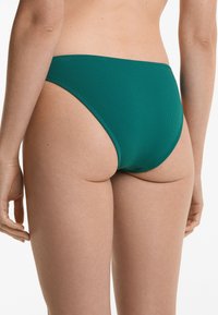 Grön bikiniunderdel i texturerad tyg, med låg midja och minimal täckning. Rena kanter utan synlig hårdvara eller detaljer.