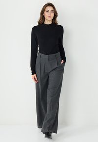 Zwarte lange mouwen top gecombineerd met hoogwater, wijde grijze geblokte broek. De broek heeft plooien en zijzakken. Klassieke schoenen maken de look compleet.