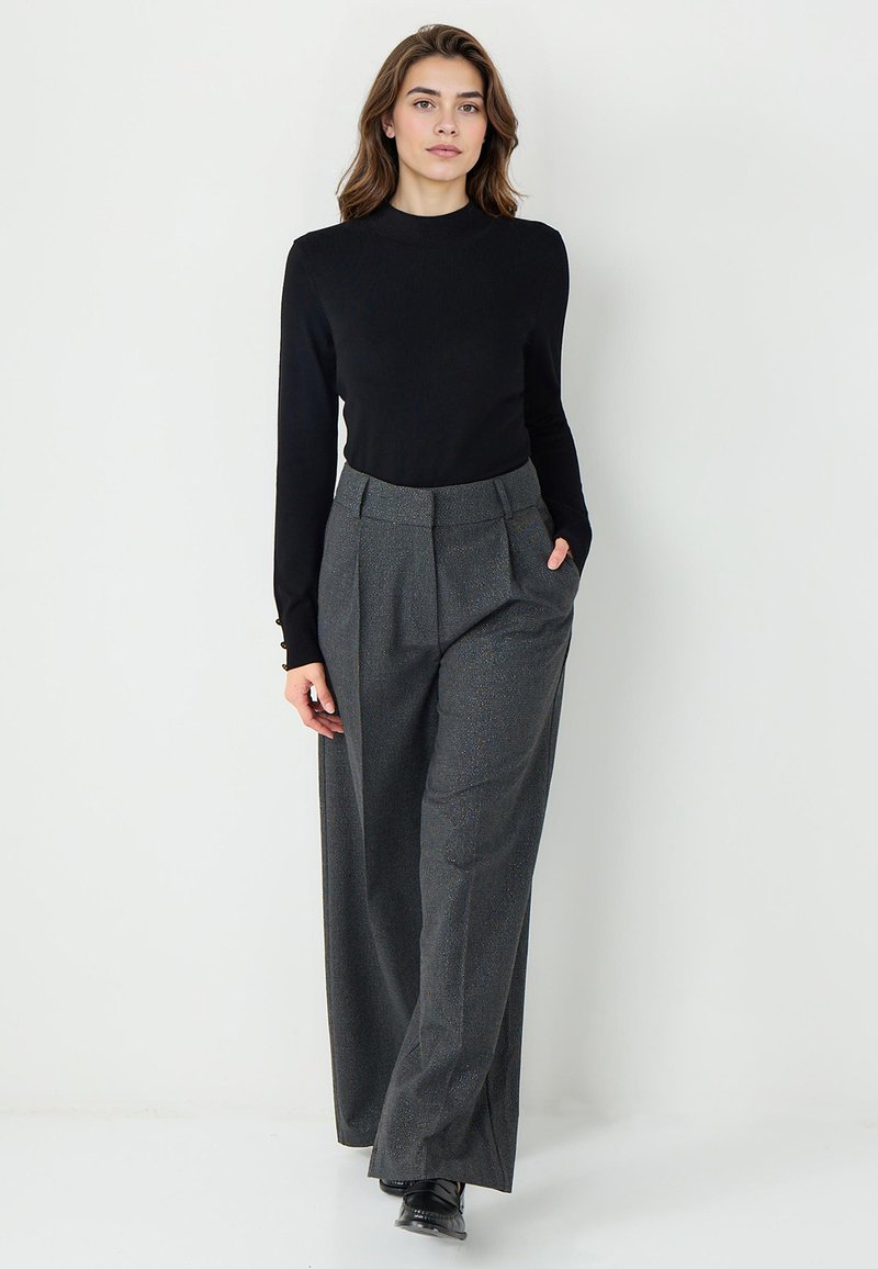 Zwarte lange mouwen top gecombineerd met hoogwater, wijde grijze geblokte broek. De broek heeft plooien en zijzakken. Klassieke schoenen maken de look compleet.