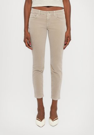 Jeans de denim bege, justos, com um design clássico de cinco bolsos, fecho de botão e pernas retas, combinados com sapatos de salto agudo brancos.