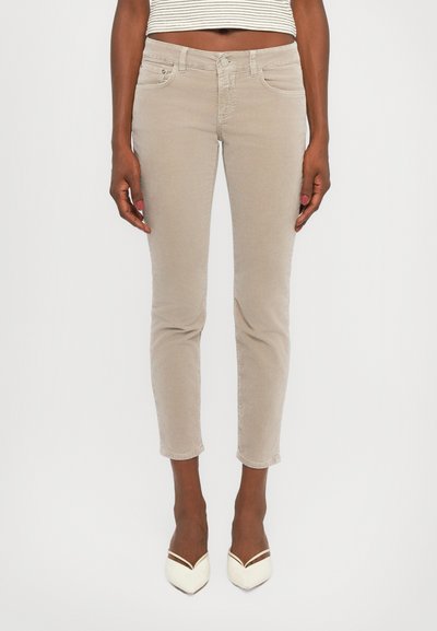 Beige, taillierte Denim-Jeans mit klassischem Fünf-Taschen-Design, Knopfverschluss und geraden Beinen, kombiniert mit weißen spitzen Absätzen.