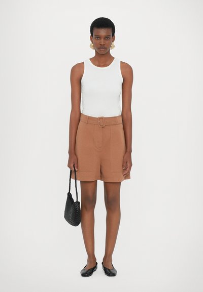 Shorts marron ceints, débardeur blanc, chaussures plates noires et sac tissé noir. Tissu lisse, coupe ajustée et design minimaliste.