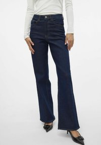 Mörkblå utsvängda jeans med hög midja, med klassisk femfickdesign och kontrasterande orange sömmar, tillverkade av denimtyg.