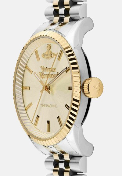 Zilveren en gouden metalen horloge met een gestructureerde gouden wijzerplaat, geribbelde bezel en opvallende uurmarkeringen. Heeft een prominent kroontje met een gegraveerd ontwerp.