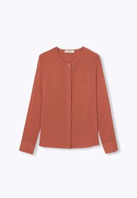 Blouse à manches longues couleur rouille avec un col rond, fermeture à boutons sur le devant et une poche poitrine unique. Texture plissée sur toute la surface.