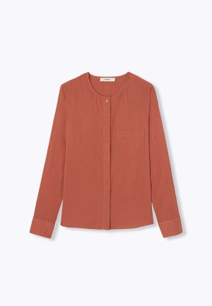 Blouse à manches longues couleur rouille avec un col rond, fermeture à boutons sur le devant et une poche poitrine unique. Texture plissée sur toute la surface.