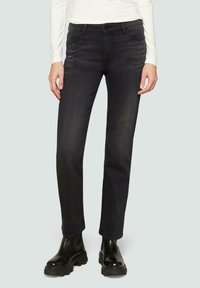 Jean en denim noir avec une coupe droite, présentant des accents métalliques sur les poches et une texture légèrement décolorée. Portés avec des bottes noires.