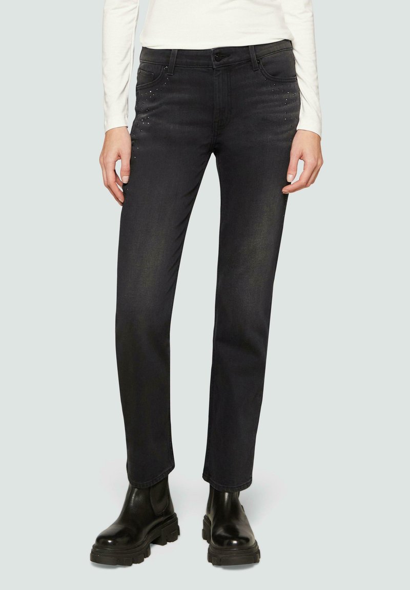 Zwarte denim jeans met een rechte snit, voorzien van metalen accenten op de zakken en een licht vervaagde textuur. Draagt met zwarte boots.