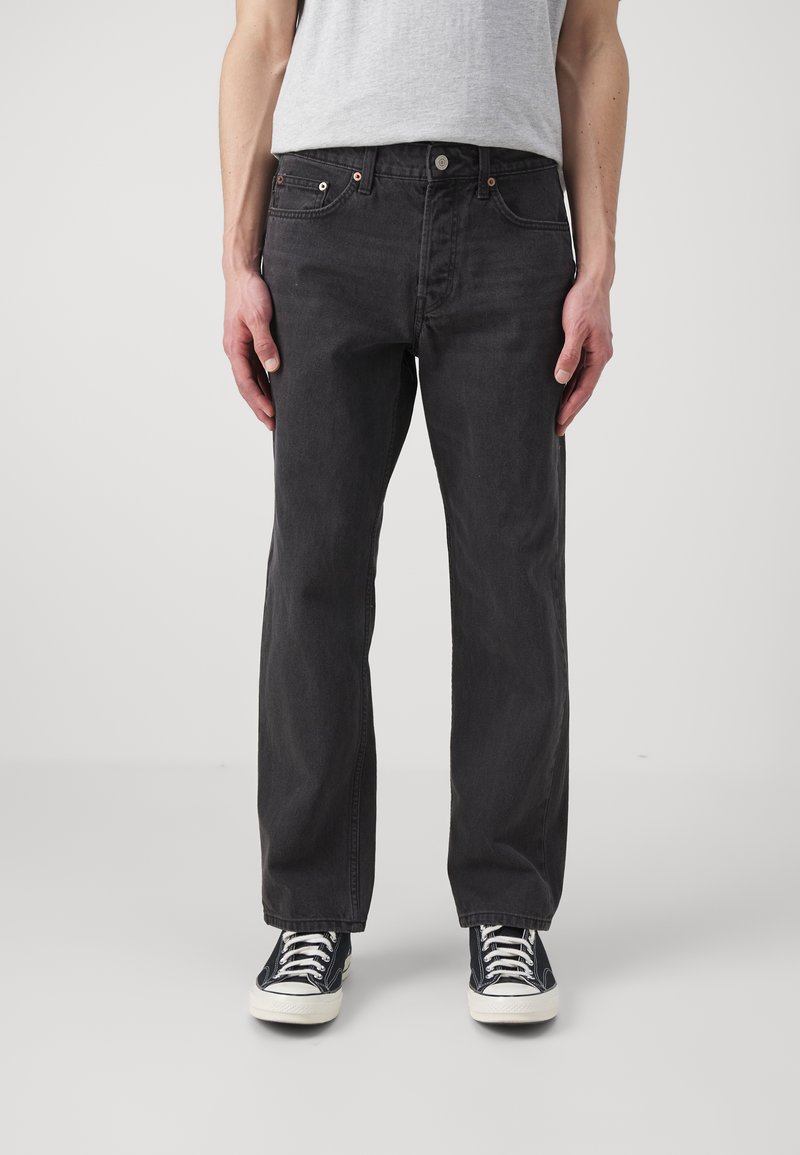 Schwarze Denim-Jeans mit geradem Bein, fünf Taschen, Kupferriegeln und dezenten Waschungen auf der Vorderseite. Tragen Sie sie mit schwarzen Turnschuhen.