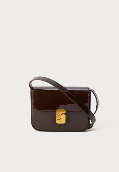 Ciemnobrązowa torebka crossbody z lakierowanej skóry z złotym geometrycznym zapięciem i wąskim paskiem, ustawiona na jednolitym białym tle.