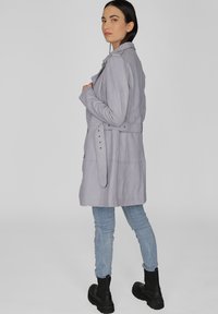 Lichtgrijze lange jas met een tailleband, knoopdetails en een kraag. Gecombineerd met lichtblauwe skinny jeans en zwarte enkellaarsjes.
