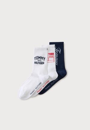 Trois paires de chaussettes Tommy Hilfiger blanches et bleu marine avec le texte de la marque et les logos visibles sur chaque paire.