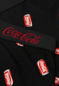 Svart tyg med ett upprepat mönster av röda Coca-Cola-burkar, med en framträdande röd Coca-Cola-logga på en svart midjeresår.