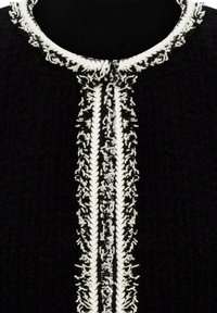 Tissu noir texturé avec une bordure tressée blanche et une broderie blanche complexe le long d'un col rond et d'une patte de boutonnage avant.