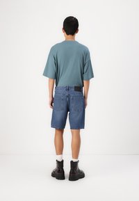 Camiseta de algodón en color aguamarina con mangas cortas, combinada con pantalones cortos de denim azul oscuro, con un corte clásico y bolsillos traseros, llevada con botas negras.