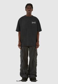 Sort oversized t-shirt med logo på brystet, parret med grå cargo bukser med flere lommer og snoretræk i kanten.