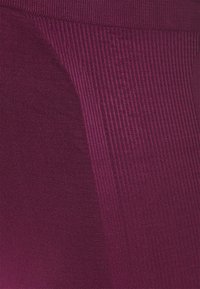 Detailní záběr na fialovou pletenou látku s hladkými a hřebínkovými texturálními vzory vytvářejícími geometrické tvary.