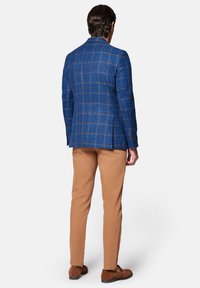 Niebieska marynarka w kratę z brązowymi akcentami, dopasowany krój, dwa rozcięcia z tyłu. W zestawie z beżowymi chinosami i brązowymi butami, widok z tyłu.