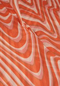 Tissu avec un motif géométrique ondulé dans des tons d'orange, de rose et de marron, présenté avec une texture visible et de légères plis.
