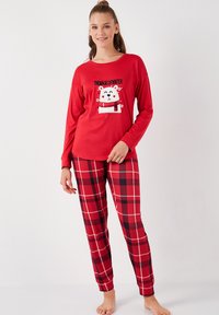 Punainen pitkähiha pyjama yläosa, jossa on karhukuva ja teksti, yhdistettynä punamustaraidallisiin housuihin, jotka on valmistettu pehmeästä kankaasta.