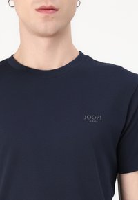 Sötétkék pamut póló kerek nyakkal. Diszkrét, világosabb árnyalatú "JOOP! JEANS" logó található rajta a mellrészen. Sima textura.