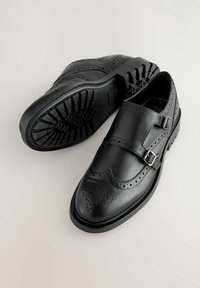 Mustat nahkakengät, joissa on brogue-muotoilu, kaksoisoljet ja teksturoidut kumipohjat, joissa on kuvioitu uritus.