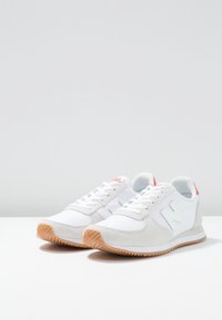 Baskets blanches de sport combinant daim et matériaux synthétiques, semelle en caoutchouc naturel, bout rond et accents rouges au niveau du talon.