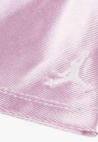 Primer plano de tela rosa brillante con textura acanalada y un pequeño logo blanco con la silueta de una persona saltando con una pelota en una mano.