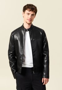 Giacca in finta pelle nera con colletto alto, chiusura con zip e inserti sulle spalle. Texture liscia e design slim fit.