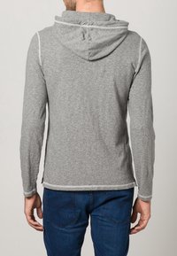 Graue Kapuzenjacke mit langen Ärmeln, aus weichem Stoff gefertigt, mit einer kontrastierenden weißen Naht entlang der Kanten und der Kapuze.