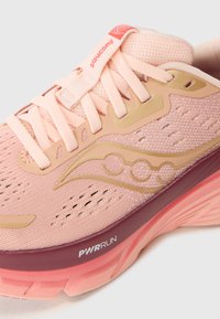 Hellrosa Sportschuh mit einem Obermaterial aus Mesh, goldenen Akzenten und einem roten Logo. Verfügt über dicke Sohlen, die mit "PWRRUN" für Dämpfung gekennzeichnet sind.