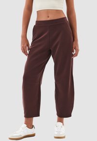 Bordeaux cropped sweatpants met een elastische tailleband, zijzakken en een gladde textuur, gecombineerd met witte sneakers en een licht bovenstuk.