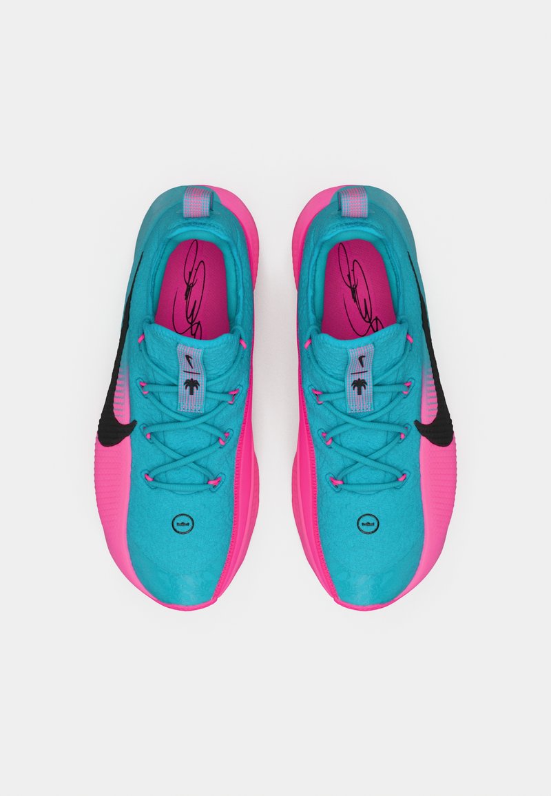 Un par de zapatos deportivos en turquesa y rosa con los swooshes negros de Nike, cordones y firma en las plantillas, vistos desde arriba sobre un fondo blanco.