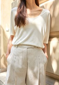 Krémová lehká košile s vykrojeným výstřihem v kombinaci s béžovými skládacími kalhotami. Přirozená textura a uvolněný střih.