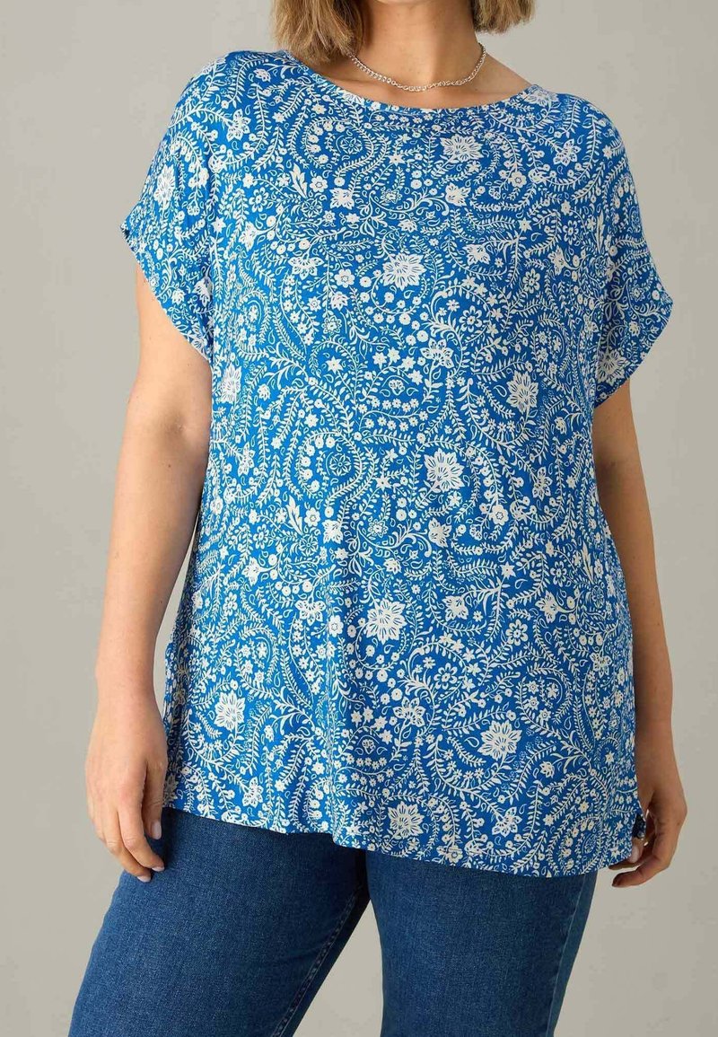 Blå blommönstrad topp med rundad halsringning, korta ärmar och en lös passform. Tillverkad av lätt tyg med en slät yta.
