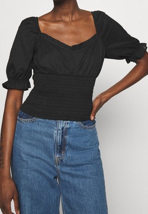 Top nero con maniche a sbuffo e scollatura quadrata, vita smock e tessuto morbido, abbinato a jeans in denim blu a vita alta con taglio classico.