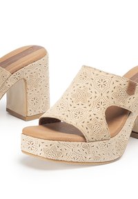 Sandalias de plataforma beige con patrones florales recortados, una parte superior texturizada y un tacón grueso. Suela lisa con acentos de aspecto madera.