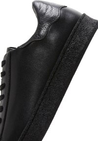 Black leather sneaker with textured black rubber sole, rounded toe, lace-up front, and a smooth, sleek upper with a padded heel section.