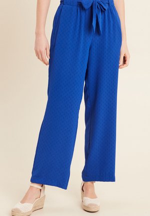 Koninklijk blauwe wijde broek met een textuurpatroon, voorzien van een strikband en zijzakken, gecombineerd met lichtgekleurde espadrilles.