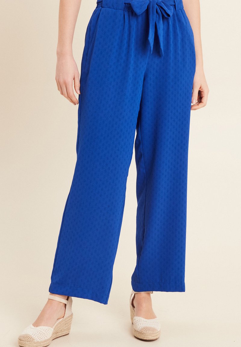 Koninklijk blauwe wijde broek met een textuurpatroon, voorzien van een strikband en zijzakken, gecombineerd met lichtgekleurde espadrilles.